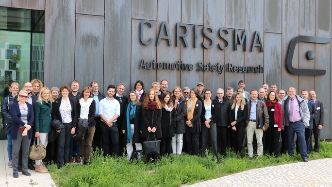 Eine Gruppe von etwa 40 Menschen versammelt sich zum Gruppenfoto vor einem Gebäude mit der Aufschrift CARISSMA Automotive Safety Research