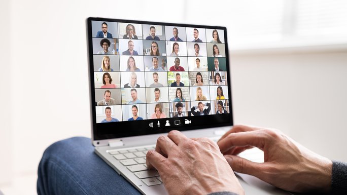 Ein Laptop mit Gesichtern in einer Videokonferenz, zwei Hände auf der Laptop-Tastatur