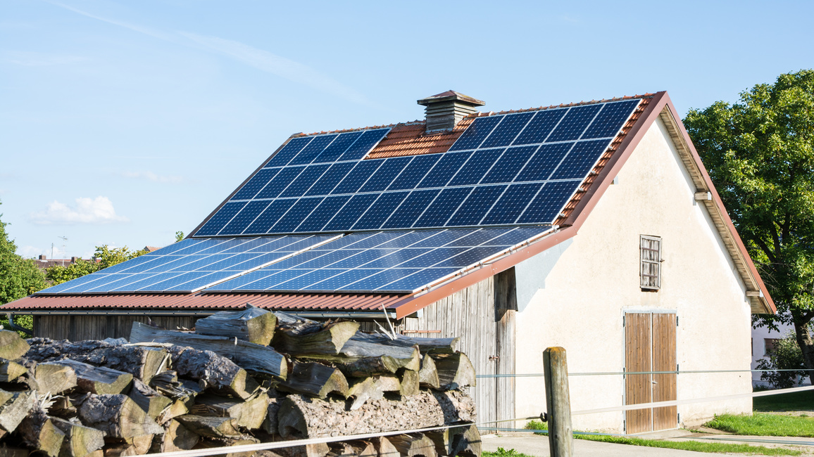 Ein Bauernhaus mit Solarzellen auf dem Dach. Im Vordergrund Holzscheite