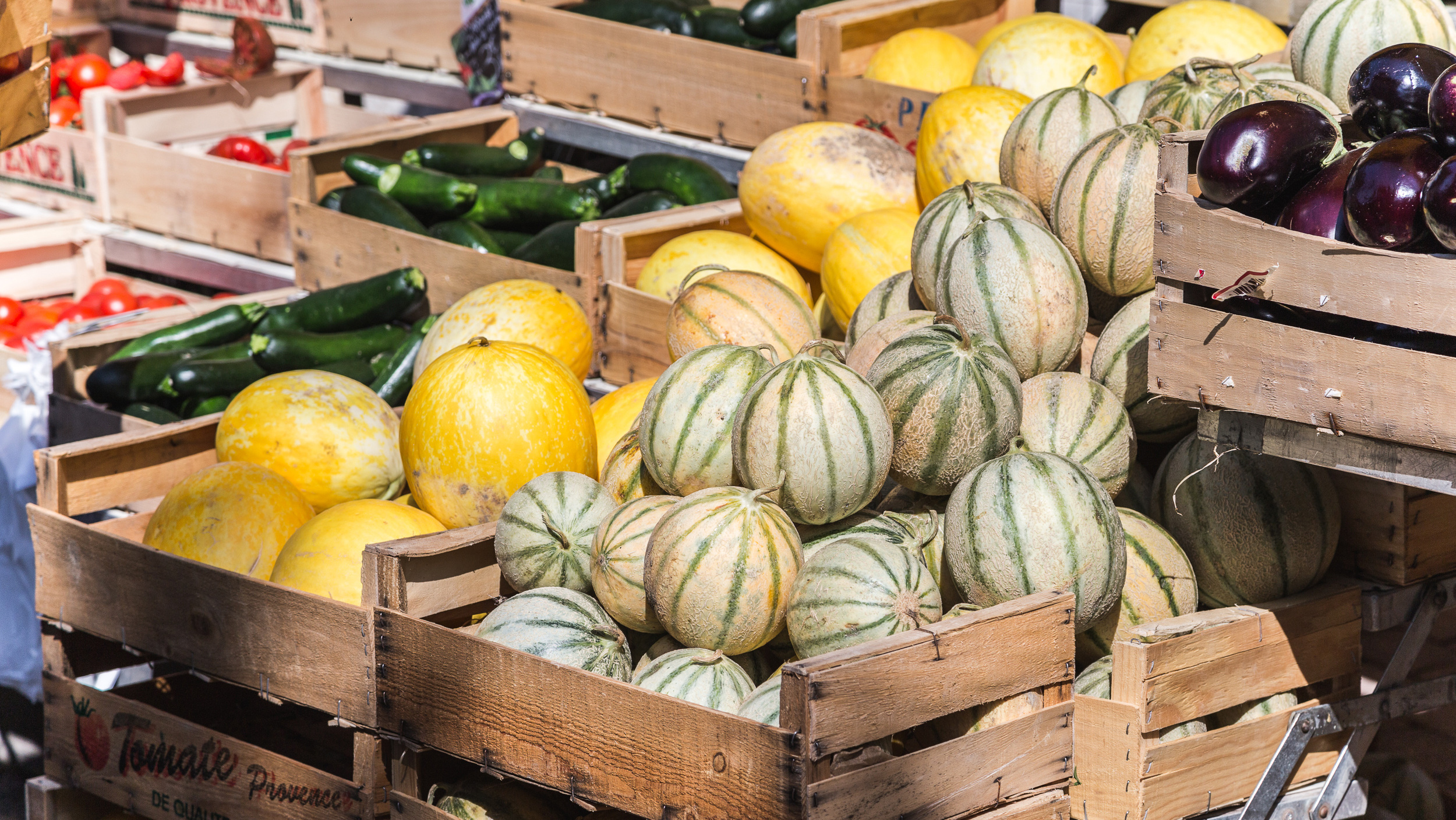 Several boxes of melons and other vegetables at a market stall