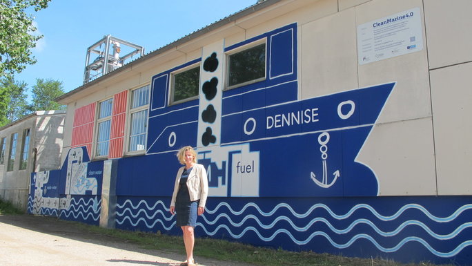 A building, painted with a ship. The leader of the CleanMarine 4.0 project stands in front of the building