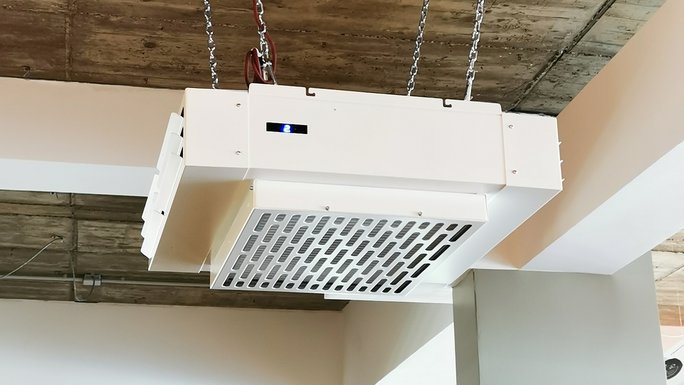 A square device with air slits is suspended from chains under the ceiling