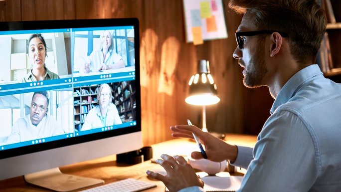A man sits in front of a screen and discusses with several people via video conference