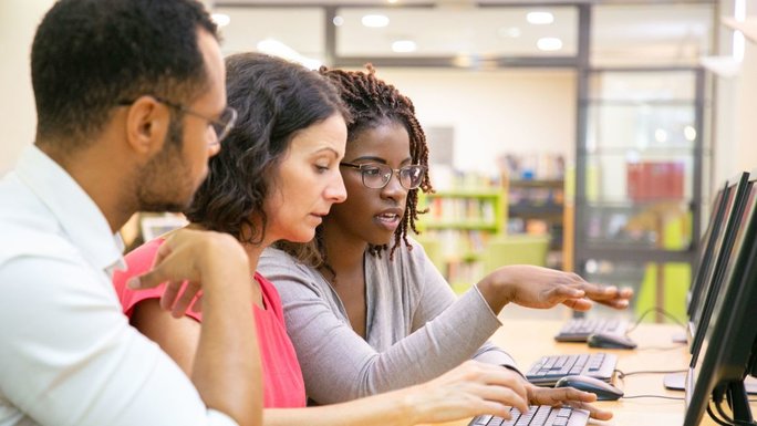 Three young people sitting in front of a PC screen and talking
