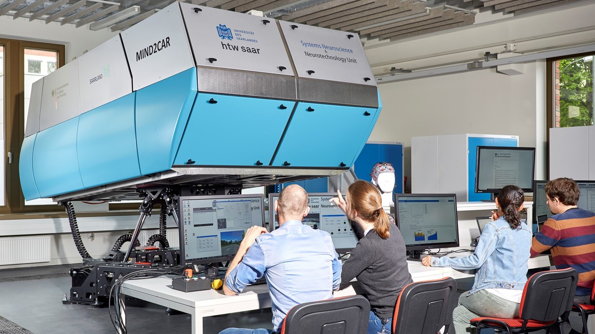 Four young researchers sitting at screens in front of a large rectangular box in turquoise and white