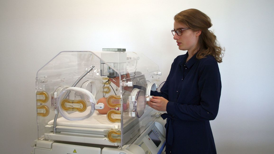A young female scientist stands next to an incubator for premature babies