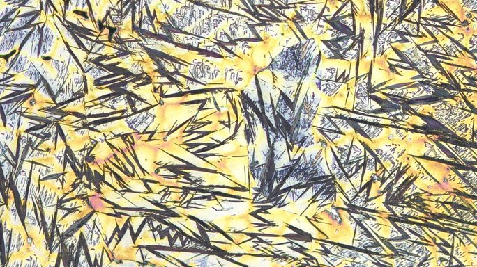 Microscopic image of metal, black zigzag lines and light blue areas on yellow background.