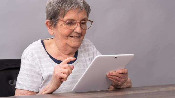 An elderly lady holds a tablet in her hand and taps on it